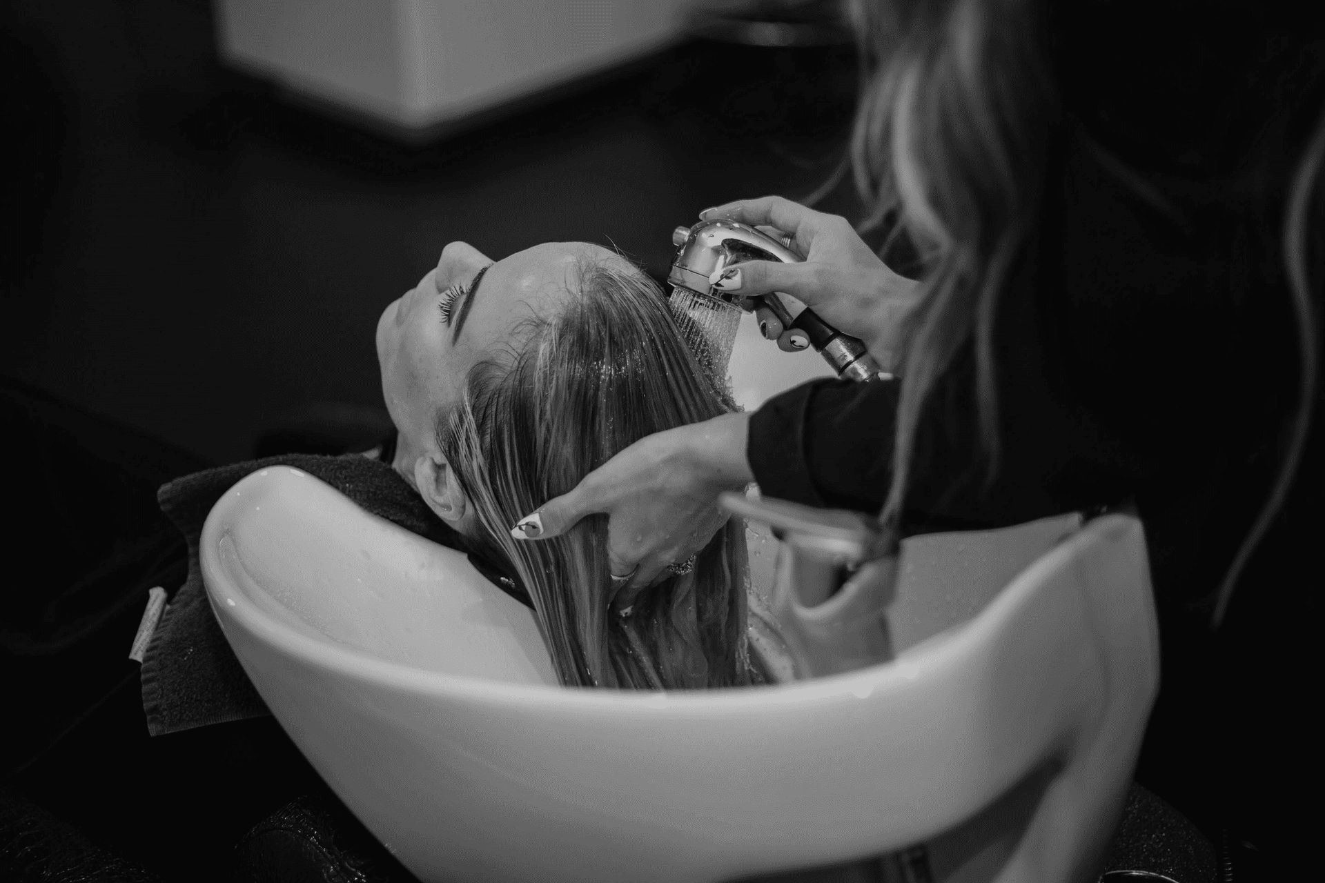 Woman getting hair washed in a salon sink by a stylist.