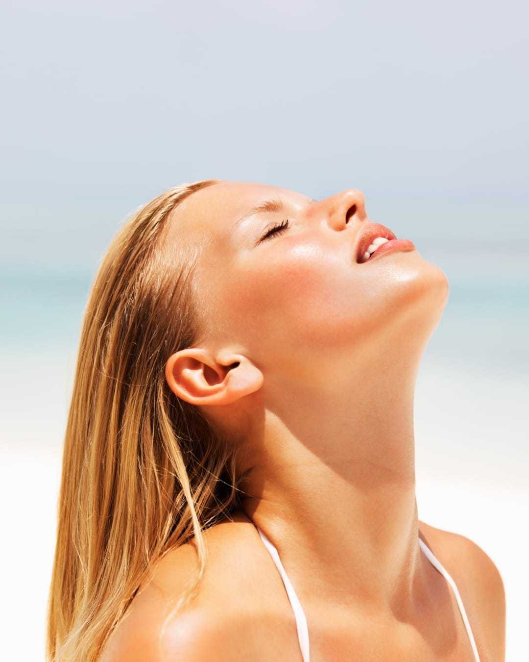 Young woman enjoying the sun on a sunny beach day, eyes closed and relaxed.