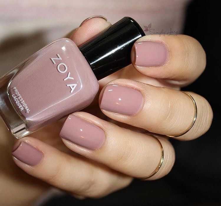 Woman's hand with shiny mauve nail polish and gold rings holding a bottle of Zoya nail polish.