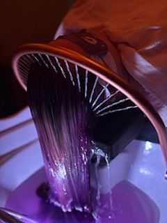 Hair being washed and rinsed with purple dye in salon setting.