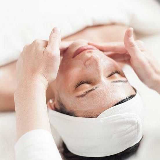 Skincare professional giving a facial massage to a woman with a headband.