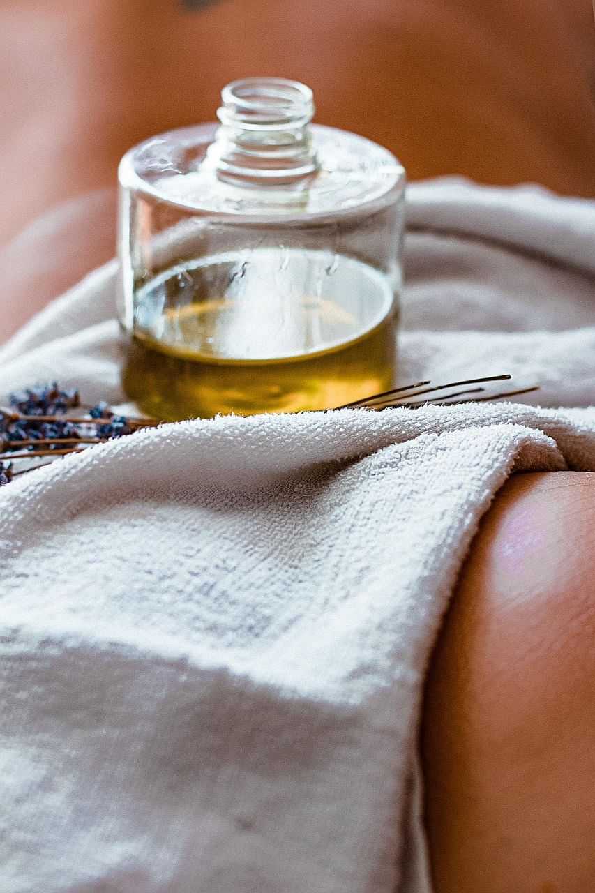 Spa treatment scene with massage oil, white towel, and lavender sprigs.