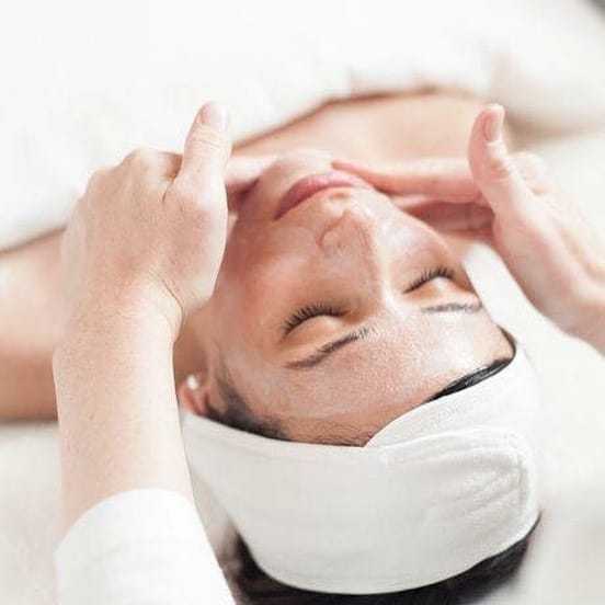 Skincare professional giving a facial massage to a woman with a headband.