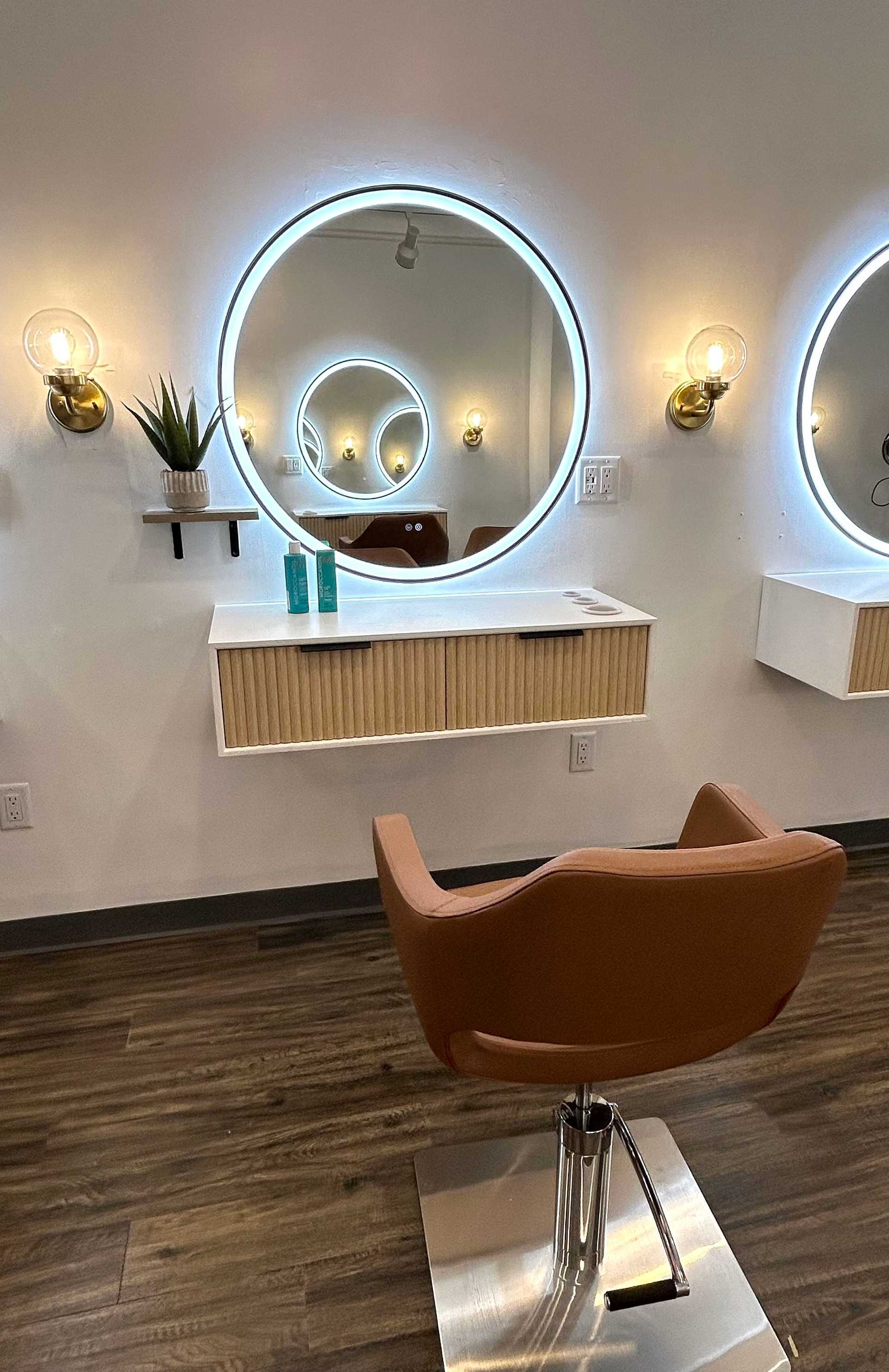 Elegant salon station with round mirror, brown chair, and decorative lighting.