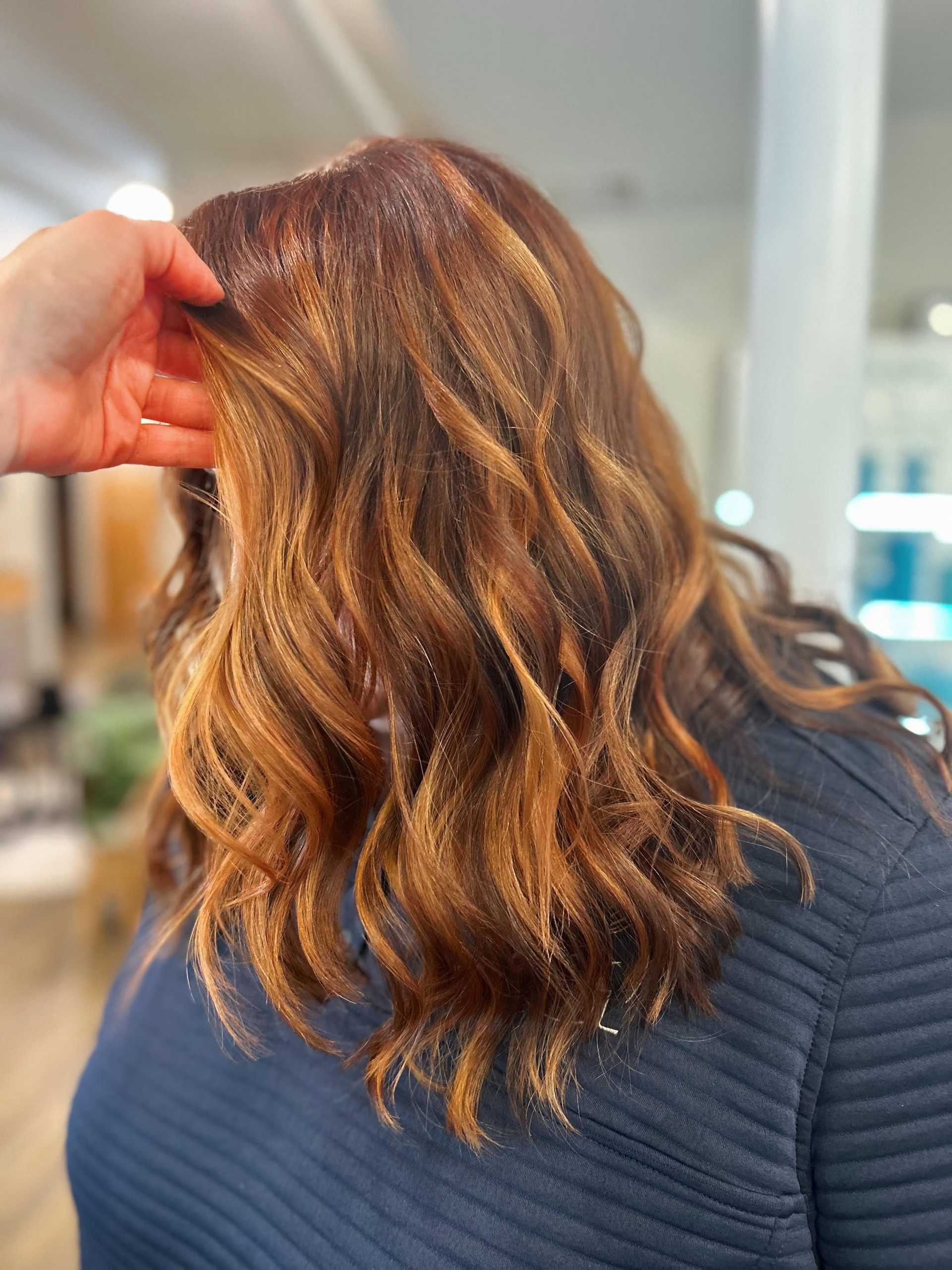 Wavy auburn hair with golden highlights styled in a salon.